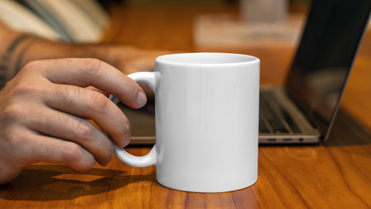 a person holding a white mug in front of a laptop