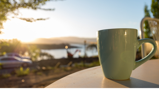 a cup of coffee sits on a table in front of a lake