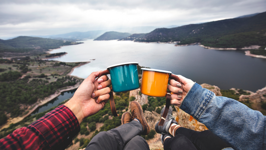 two people holding coffee cups on top of a mountain