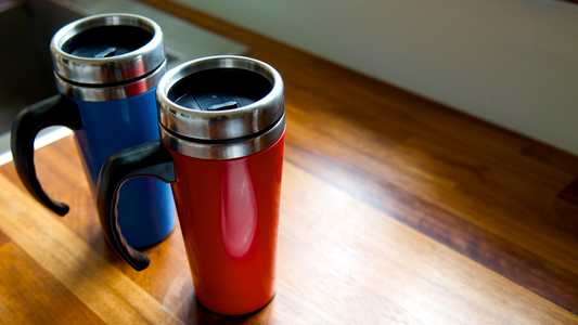 two red and blue travel mugs sitting on a wooden table