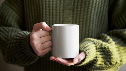 a person in a green sweater holding a white mug