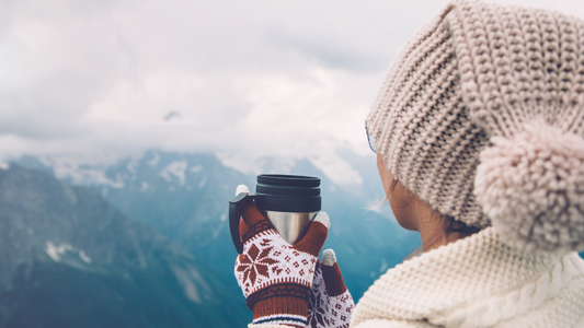 A person holding a cup of coffee on top of a mountain