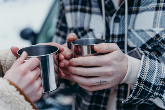 two people holding stainless steel mugs in front of a car